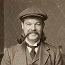 Altes Foto von Fritze 'Fresse' Lingerschreib. Ein Mann mit Schiebermütze, opulentem Schnauzbart und Pfeife grinst unwissend