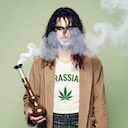 Sir Jonny Reis - ein Mann mit langen Haaren, Morgenmantel,
                     karrierten Shorts und Schlappen. Auf seinem T-Shirt steht das Wort 'GRASSIAS',
                     darunter ist ein Hanfblatt. Er hält einen rauchenden Bong in der Hand